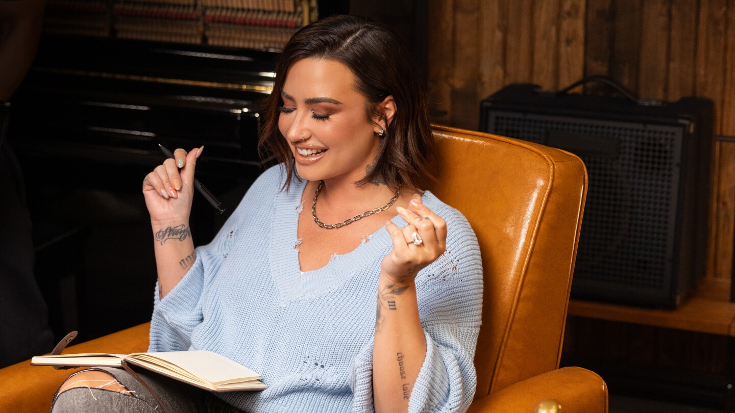 Demi Lovato è seduta con una penna in mano e i prodotti OGX nelle vicinanze